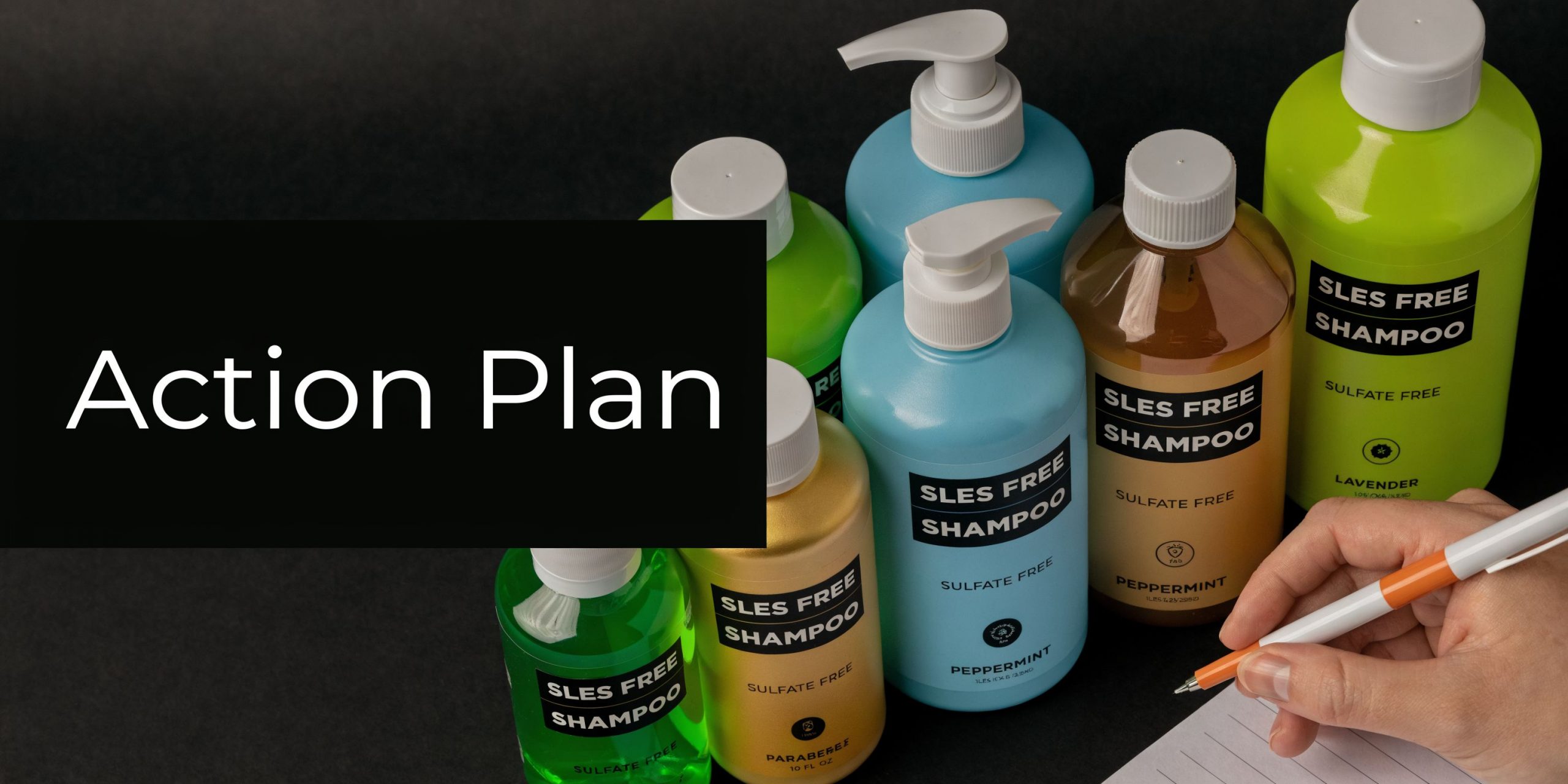 A hand writes on a notepad next to several bottles of SLES-free shampoo on a black surface.