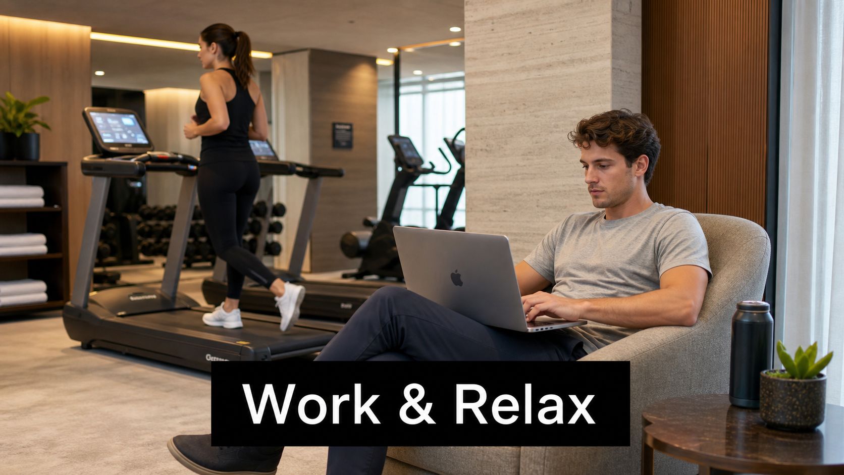A man working on a laptop in a modern gym while a woman runs on a treadmill.